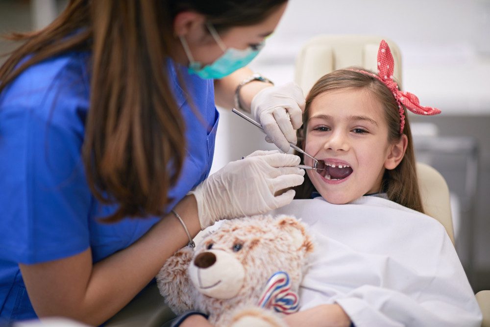 Little girl having her teeth checked as her teddy bear keeps her company